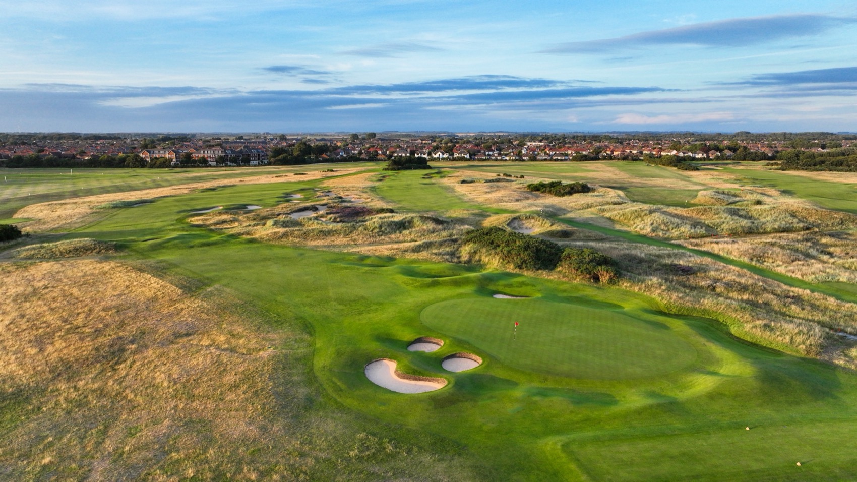 Aerial view of a Royal Lytham green ringed by bunkers and dune grass, under a blue sky